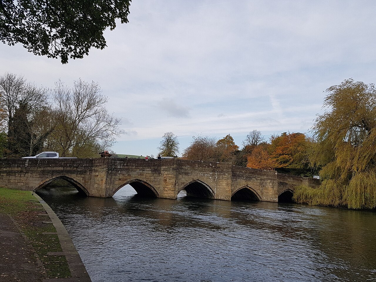 Stone arches of Bakewell Bridge over the River Wye with autumn trees beside the water