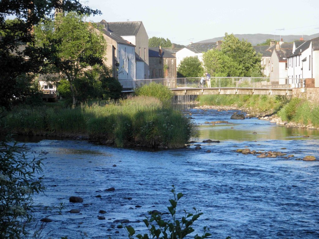 The river confluence and a footbridge between stone buildings in Cockermouth