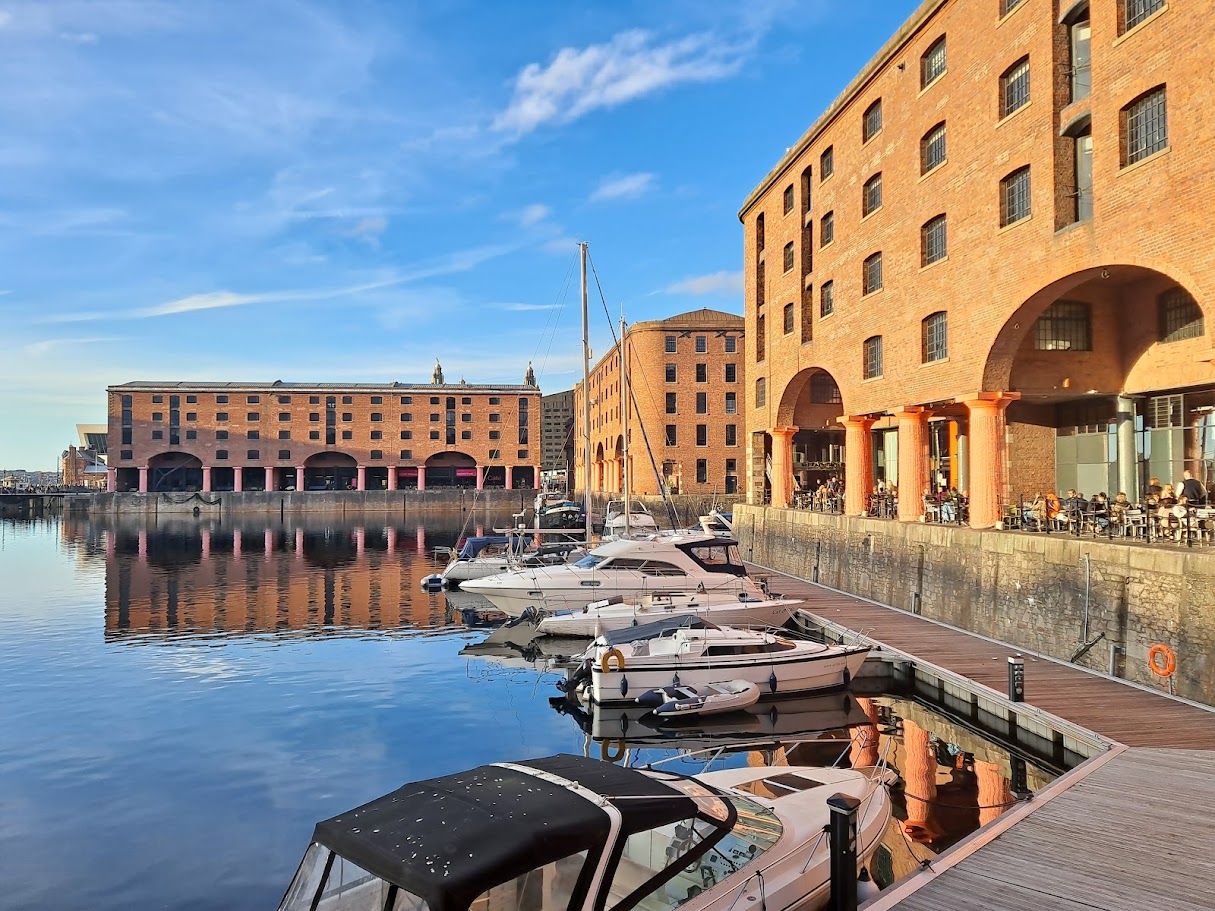 Boats moored beside the brick warehouses and reflected arches of Royal Albert Dock