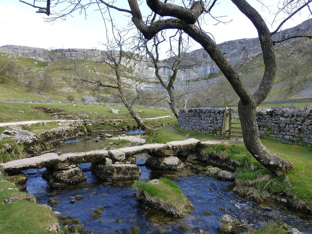 Stone clapper bridge over Malham Beck with limestone cliffs beyond