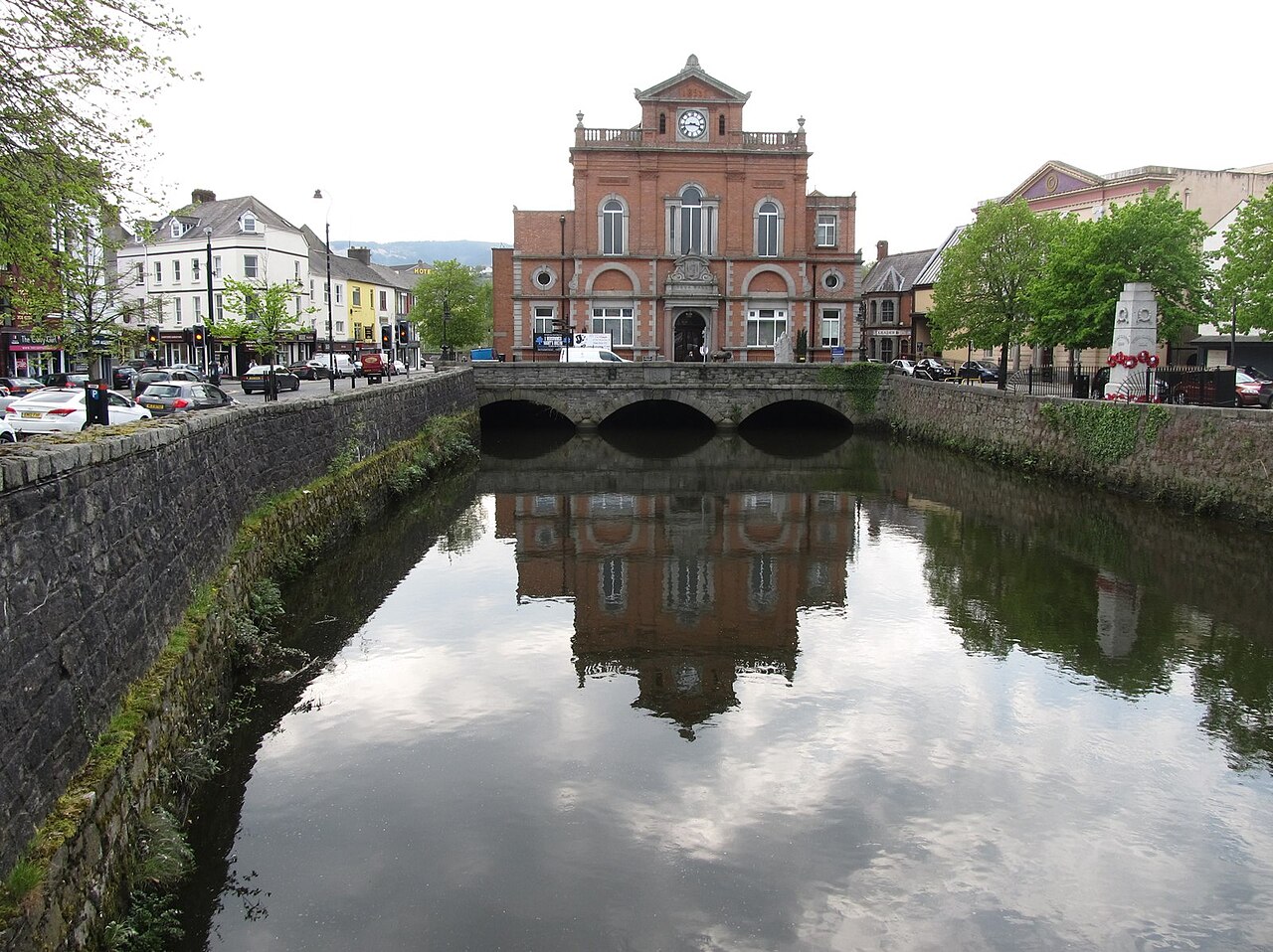 Newry Town Hall and its reflection in the central river, with stone quays and trees