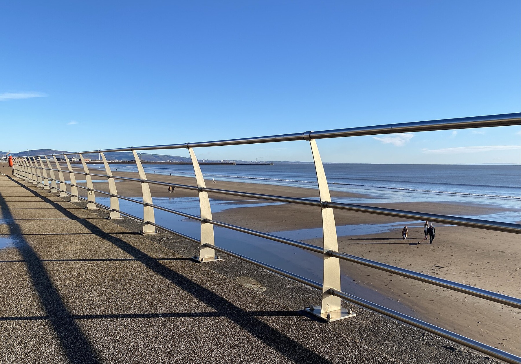 Promenade railings beside the beach and open water of Swansea Bay